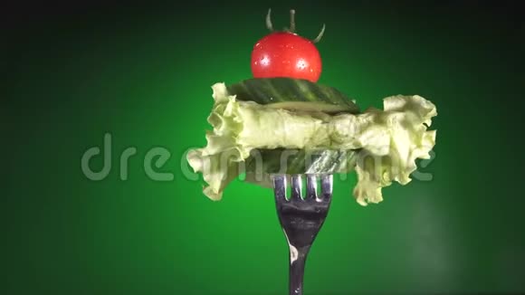 用新鲜的红番茄和黄瓜在水滴里叉生菜旋转绿色背景视频的预览图