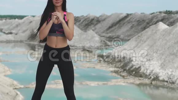 穿着黑色运动服的运动型黑发女孩在一个白色粉笔采石场和蓝色的水对抗蹲下视频的预览图