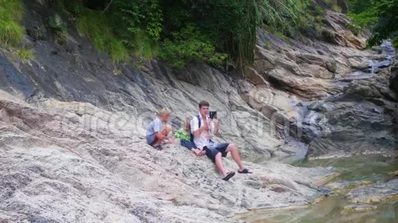 一家人坐在一条山河的岸边在智能手机上拍照视频的预览图