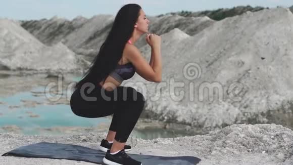 穿着黑色运动服的运动型黑发女孩在一个白色粉笔采石场和蓝色的水对抗蹲下视频的预览图