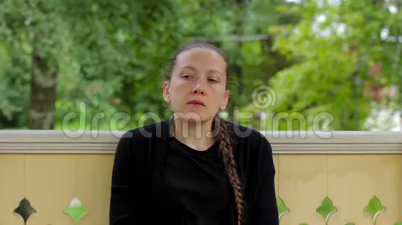 一个穿着黑色辫子的忧郁女孩坐在凉亭里的画像视频的预览图