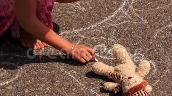 女人蹲在玩具熊的人行道上用粉笔画画视频的预览图