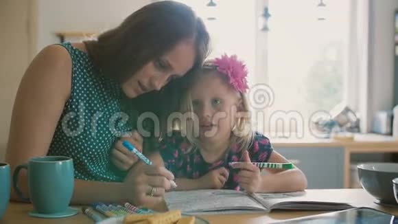 美丽的年轻母亲正在帮助她的金发小女儿用毛毡笔给一张照片上色慢节奏视频的预览图