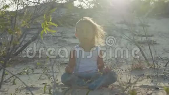 小女孩在沙漠里冥想日落时坐在沙滩上的孩子温暖视频的预览图