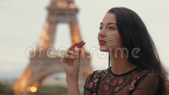 巴黎女人微笑着吃着巴黎艾菲尔铁塔上的法国糕点通心粉视频的预览图