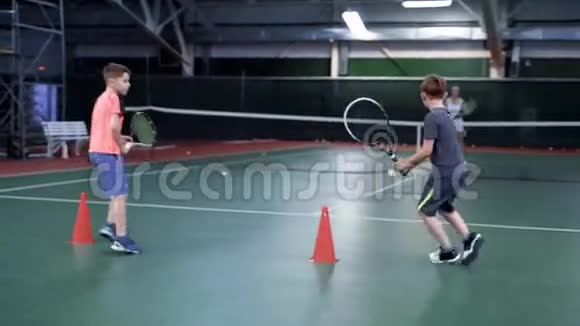 两个男孩和年长的女孩或教练打网球法庭上的体育实践视频的预览图