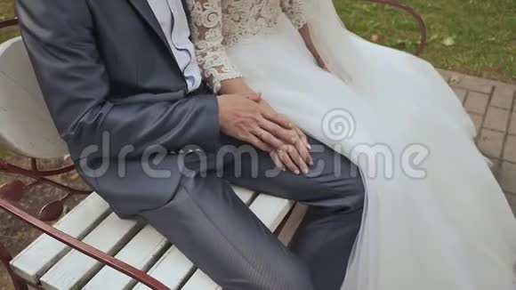 新娘和迷人的新娘坐在长凳上的绿色公园里他握着她的手结婚时尚夏天这就是视频的预览图