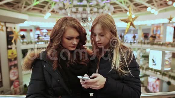 两个少女在商城饶有兴致的看着手机屏幕他们穿着夹克视频的预览图