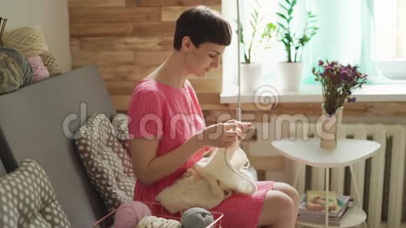 有创意的女人坐在背景窗的沙发上编织羊毛视频的预览图