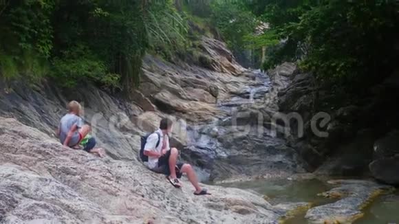 一家人坐在一条山河的岸边在智能手机上拍照视频的预览图