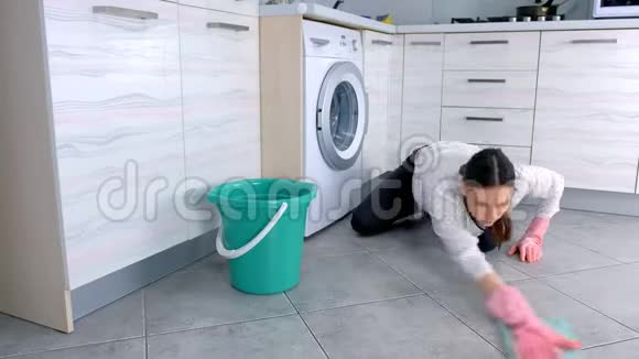 穿着粉红色橡胶手套的女人用布洗厨房地板地板上的灰色瓷砖视频的预览图