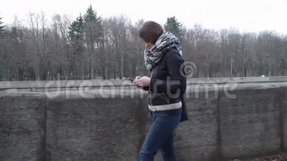 带着智能手机沿着河堤行走的女人视频的预览图