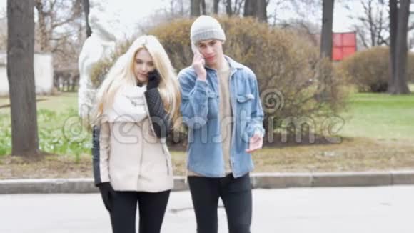两个年轻人一个漂亮的金发女郎和她的朋友正在街上走着用着手机视频的预览图