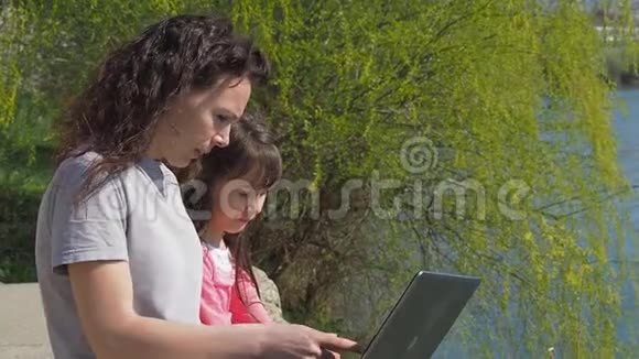 有婴儿和笔记本电脑的女人河岸上的幸福家庭妈妈在用笔记本电脑教孩子视频的预览图