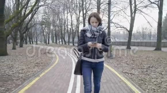 带着智能手机在城市公园散步的女人视频的预览图