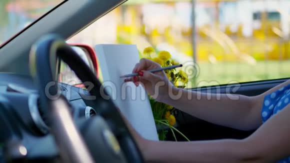 艺术家美丽的黑发女人坐在车里画铅笔素描画一束黄色的蒲公英由视频的预览图