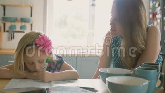 母亲正微笑着和她的小女儿说话她正在厨房桌子上画一幅画慢节奏视频的预览图