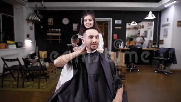 理发师的女人向坐在沙龙里的客户展示理发结果视频的预览图