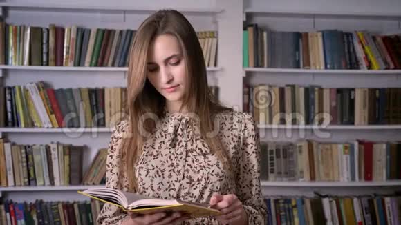 年轻漂亮的女人正在看书在镜头前看书在后台看图书馆视频的预览图