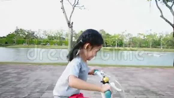 一个亚洲小女孩骑着自行车在公共公园里带着摄像机视频的预览图