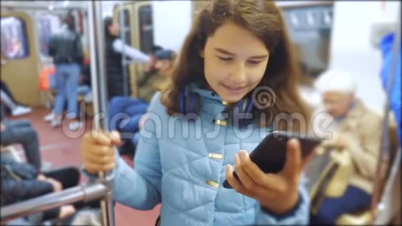 十几岁的女孩带着智能手机和耳机在地铁里很多人挤在地铁里地铁视频的预览图