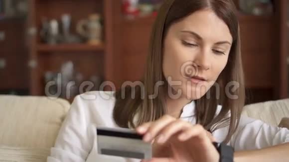 慢动作女人穿着白色衬衫坐在客厅沙发上用智能手机刷卡上网视频的预览图