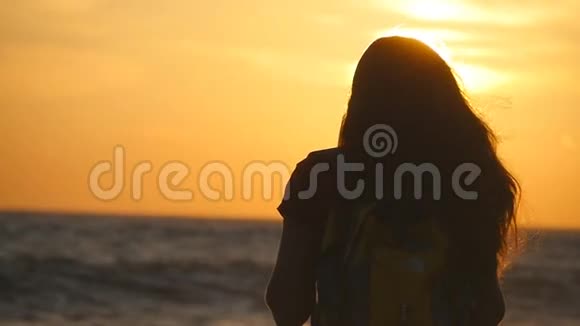 年轻的旅行者女人站在海边看日出年轻的女游客带着背包欣赏风景视频的预览图