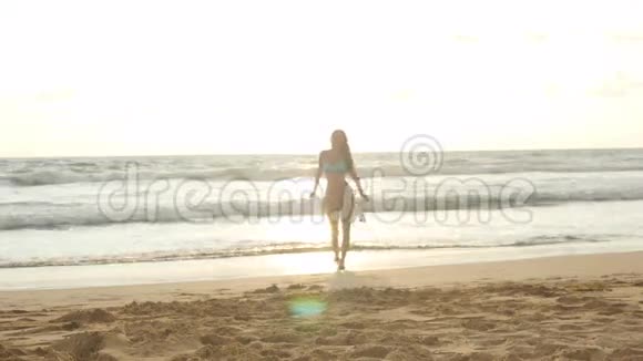 日落时分带着围巾的年轻快乐的女人沿着海边散步喜欢夏天的女孩穿比基尼的女性视频的预览图