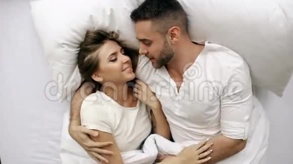 年轻美丽而有爱心的一对夫妇在早上醒来时交谈并拥抱在床上迷人的男人的俯视图视频的预览图