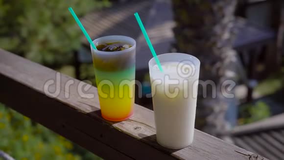 在阳光明媚的阳台上一杯多汁的分层鸡尾酒和一杯牛奶混合饮料站在扶手里视频的预览图