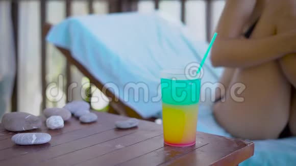 身材苗条的年轻女子穿着黑色比基尼正坐在夏日的日光浴床上女子手拿着玻璃视频的预览图