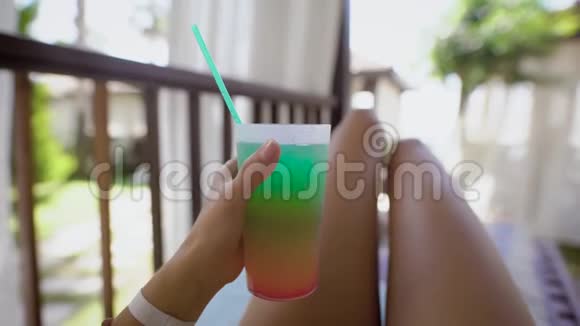 苗条的黝黑女人的腿和手拿着装有吸管的鸡尾酒的杯子女人躺在阳光明媚的躺椅上视频的预览图