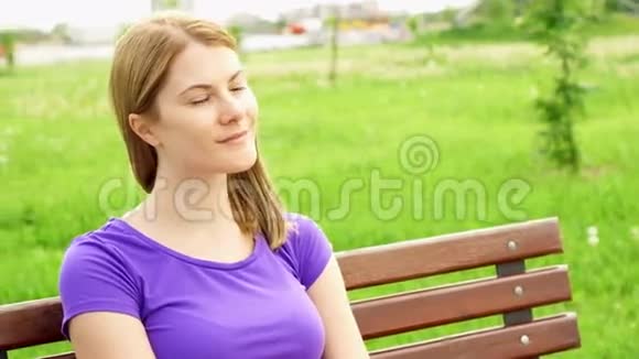 慢动作快乐微笑年轻女人享受自然坐在绿色公园的长凳上自由孤独概念视频的预览图