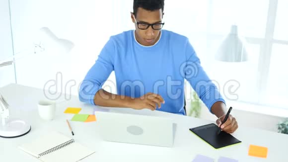 美国黑人创意设计师用笔记本电脑上的平板电脑绘制视频的预览图
