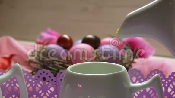 在彩色粉红色复活节彩蛋的背景下一杯茶倒在杯子里视频的预览图