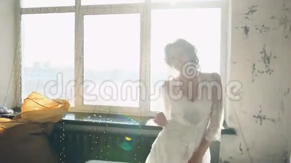 美丽的年轻新娘在镜头中跳舞和微笑的肖像女人坐在卧室的床上视频的预览图