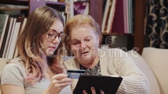 帮助祖母使用数码平板电脑和信用卡的年轻女子视频的预览图