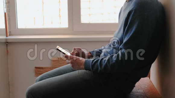 有电话的人无法辨认的年轻人坐在靠近窗户的阳台上用手机浏览互联网页面视频的预览图