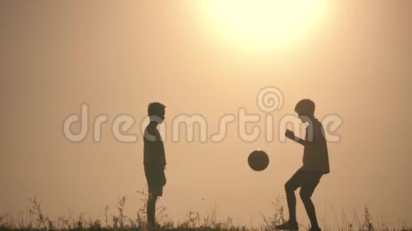 两个男孩在日落时踢足球日落时孩子们玩球的剪影幸福家庭的概念视频的预览图