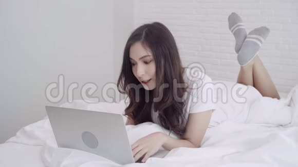 美丽的亚洲混血白人妇女使用电脑或笔记本电脑而躺在床上在她的卧室视频的预览图