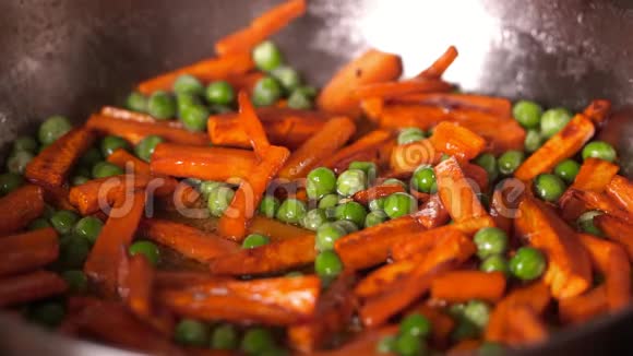 橙胡萝卜与冷冻豌豆和硅果酱接近在一个煎锅木铲搅动蔬菜视频的预览图