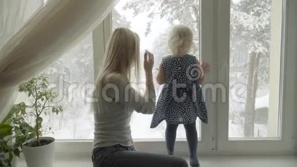 母亲正透过窗户向她的小女儿展示冬天的景色视频的预览图