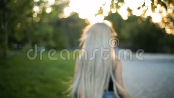 年轻的金发女郎留着一头飘逸的长发在公园里奔跑向夕阳西下视频的预览图