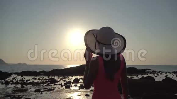 戴帽子的女孩在日落时漫步在海滩上视频的预览图