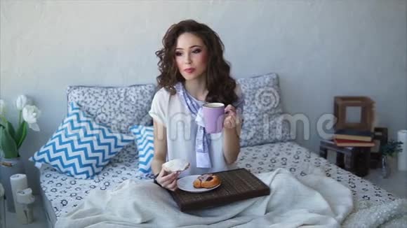年轻的女人在床上的卧室里吃早餐面包和茶视频的预览图