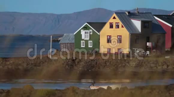 一个男人坐在一张长凳上靠近五颜六色的冰岛房屋安德列夫视频的预览图