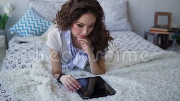 漂亮的女人在家里坐在床上使用平板电脑在线购物视频的预览图