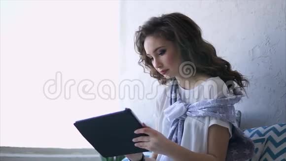 漂亮的女人在互联网上工作在客厅的平板电脑上使用无线网络视频的预览图