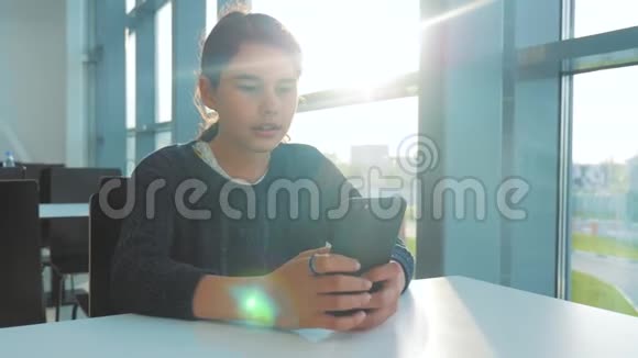 十几岁的女孩正在聊天在一个餐桌上的生活方式阳光下在一家咖啡馆里用智能手机与信使交流视频的预览图