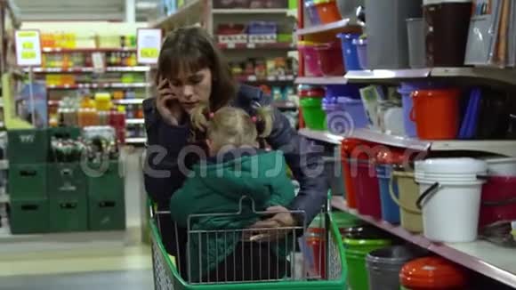 一个年轻的女人带着一个孩子在超市选择商品妈妈在手推车上驾驶一个小女孩考虑一下货物视频的预览图